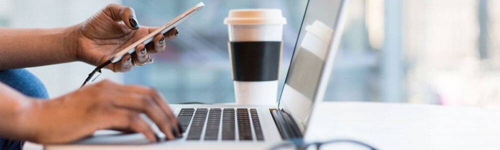 Person sitting at their desk in front of screen looking at their phone